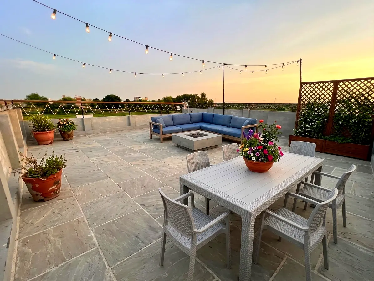 Rooftop seating at dusk with string lights, sofa, fire pit and dining table overlooking the fields